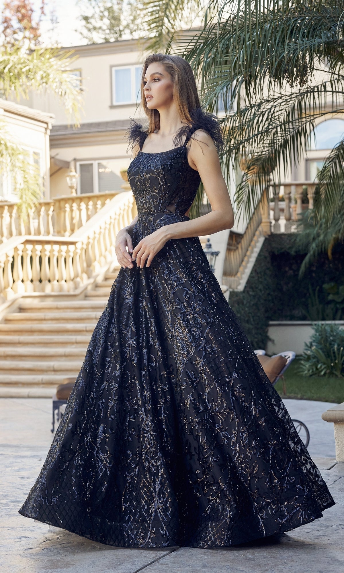 A woman stands outdoors in the Feathered-Cap-Sleeve Long Sequin Prom Ball Gown 297, featuring a full skirt and sparkling details, with stairs and lush greenery in the background.